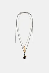 Pack de dos collares. El primero es un collar de cordón negro ajustable con colgantes: una pieza redonda marrón carey, una gota dorada y una gota plateada. El segundo es una cadena fina dorada con un dije alargado dorado y un dije pequeño plateado.