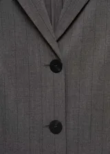 Vestido corto entallado de estilo chaleco, color gris con sutil estampado de rayas verticales. Presenta cuello con solapas, cierre frontal con botones y diseño sin mangas.