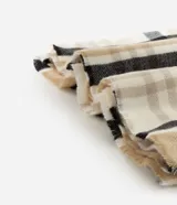 Bufanda de punto suave con estampado de cuadros en tonos beige, blanco y negro, con terminaciones de flecos en los extremos.