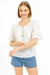 Camisa de viscosa blanca con broderie floral, cuello redondo con cordones ajustables y mangas cortas acampanadas.