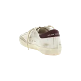 Championes Golden Goose de corte bajo, color blanco con efecto desgastado, estrella lateral y talón en tono bordó, con cordones beige.