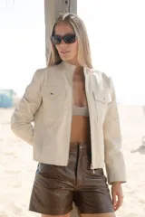 Campera corta color arena confeccionada en cuero ovino italiano, con cuello mao, cierre metálico frontal, bolsillos laterales y bolsillos falsos con solapa y broches a la altura del busto.