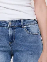 Jean wide leg de tiro medio, color azul claro, confeccionado en denim de algodón con un toque de elastano. Cuenta con cinco bolsillos, presillas para cinturón y cierre frontal con botón. El diseño destaca por su pretina regulable con cruce y broches metálicos.