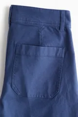 Pantalón de tiro alto confeccionado en lona de algodón, con diseño de pierna recta, raya marcada en el frente y la espalda, cierre con botones metálicos y bolsillos de parche en la parte posterior.