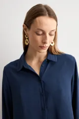 Camisa de corte clásico y calce holgado, con cuello camisero, cierre frontal de botones y mangas largas con puños abotonados.