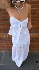 Pollera larga de encaje blanco con volados en el ruedo. Tiene un top a juego con breteles finos y volados en el busto, con un lazo en el centro.