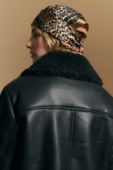 Campera tipo gamulán de cuero sintético negro, con interior y detalles de corderito sintético al tono en cuello y ruedo. Presenta cierre frontal metálico y diseño de silueta relajada.