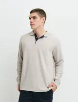 Remera de manga larga con cuello polo, confeccionada en tejido de punto canalé francés. Presenta abotonadura frontal con botones de madera y detalles a contratono en la cartera y el interior del cuello.