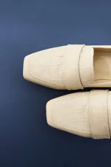 Mocasines de cuero vacuno color beige con textura efecto cocodrilo, punta cuadrada y taco bajo.