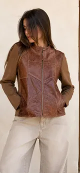 Campera con frente de cuero en tono marrón con diseño de paneles geométricos y mangas de lana merino en color marrón. Presenta cuello redondo con cierre de broche y cierre frontal completo.