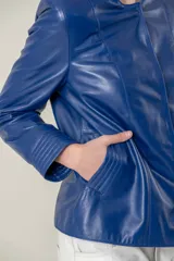 Campera de cuero ovino italiano color verde azulado, con cuello mao, cierre frontal con broches ocultos, bolsillos laterales y detalle de capitoneado en puños y bolsillos.