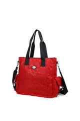 Cartera tipo tote bag color rojo, confeccionada en material sintético con estampado de corazones y letras en tono sobre tono. Cuenta con doble asa superior de cinta negra con inscripciones, correa ajustable y extraíble, bolsillos laterales y un aplique metálico con logo en el frente.