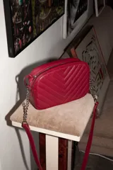 Cartera bandolera negra con diseño capitoneado en forma de V, correa de cuero y cadena plateada, cierre metálico y doble bolsillo interior.