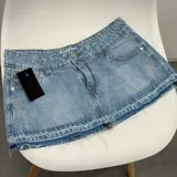 Minifalda de denim de tiro medio, color celeste con lavado ácido. Cuenta con bolsillos traseros con apliques de strass en forma de rayo, trabillas para cinturón y ruedo desmechado.