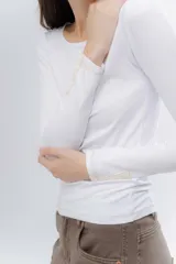 Remera básica de manga larga en color gris melange, confeccionada en algodón suave. Presenta un diseño de cuello redondo y un detalle de etiqueta decorativa en el puño.