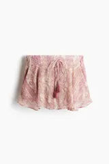 Short de tejido liviano con estampado paisley en tonos rosados y crema. Presenta un corte holgado, tiro alto, pretina con elástico en la parte posterior y cordón frontal ajustable con borlas y cuentas decorativas.