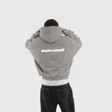 Hoodie gris de corte holgado con capucha y bolsillo frontal tipo canguro. Presenta un estampado gráfico en color blanco en la espalda con la inscripción weare.venefö.