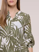 Vestido midi de silueta holgada en color blanco con estampado de hojas verdes. Presenta escote en V con cuello mao y botones frontales en la pechera, mangas tres cuartos abullonadas con puños elásticos y falda de corte evasé con niveles fruncidos.