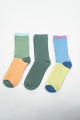 Pack de tres pares de medias de caña media con diseños coloridos. Un par es verde con celeste y naranja, otro par es verde liso, y el tercero es celeste con lila, amarillo y azul.