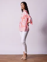 Blusa color salmón con estampado floral blanco, cuello redondo con abertura y mangas 3/4 acampanadas.