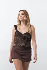 Top sin mangas color marrón oscuro, con escote en V, cruce frontal y breteles con volados. Confeccionado en tejido liviano con textura aterciopelada y estampado floral, de calce entallado y elastizado.