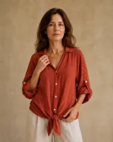 Camisa de lino color terracota, de corte holgado, con cuello camisero, cierre frontal de botones y mangas largas con detalles perforados y trabilla para arremangar.