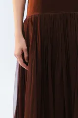 Vestido largo negro con breteles finos y escote recto, parte superior lisa y falda amplia de pliegues finos con gran movimiento y caída.