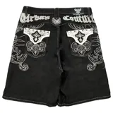 Bermuda de denim negro con bordados blancos estilo barroco/rococó en los bolsillos traseros y a lo largo de los costados. Presenta costuras contrastantes blancas, tiro medio y calce holgado (baggy fit). En la parte superior trasera lleva un aplique con el texto "Urban Coutur".