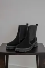 Bota corta negra de gamuza y neopreno, con elástico lateral y costuras blancas. Tiene suela track y tirador trasero.