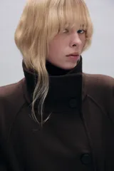 Abrigo largo confeccionado en hilatura con lana, de corte recto y diseño estructurado. Presenta cuello subido, manga larga, bolsillos delanteros de vivo y cierre frontal con botones. Incluye un cinturón del mismo tejido para ajustar a la cintura y abertura en la espalda.