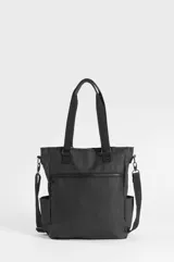 Bolso tipo tote negro confeccionado en PVC y poliéster, con compartimento principal con cierre, bolsillos laterales y bolsillo trasero con cierre. Incluye asas superiores de mano, correa ajustable removible y un estuche removible para paleta de pádel con detalle de franja vertical blanca.