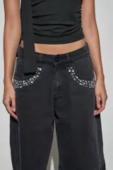 Bermuda de denim negro con diseño holgado, tiro medio y detalles de tachas y strass aplicados en los bolsillos delanteros. Presenta terminaciones deshilachadas en las piernas.