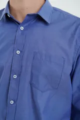 Camisa azul de manga larga con cuello clásico, cierre con botones y bolsillo en el pecho.