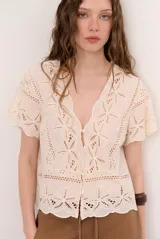 Camisa azul de manga corta confeccionada en tejido broderie con diseño calado y floral. Cuenta con escote en V y cierre frontal de botones.