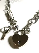 Collar plateado con cadena de eslabones, detalles de acero quirúrgico hipoalergénico y dije de candado con forma de corazón y llave.