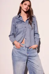 Camisa de denim celeste con cuello clásico, cierre frontal con botones a presión, dos bolsillos con solapa abotonada en el pecho y mangas largas con puños abotonados.