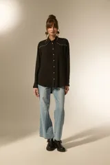Camisa negra de viscosa con corte holgado, cuello clásico, cierre frontal de botones y detalle de tachas metálicas en la línea de los hombros.