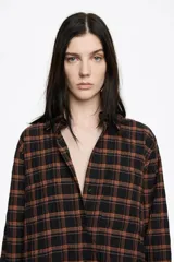 Camisa de corte recto y largo medio, confeccionada en tejido de algodón con textura. Presenta un diseño de cuadros en tonos rojo, negro y azul, cuello camisero, cierre frontal con botones, manga larga con puños abotonados y bolsillo de plastrón en el pecho.