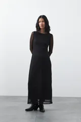 Vestido largo de manga larga confeccionado en tejido de malla transparente con sutil textura. Presenta un diseño entallado, cuello redondo y una silueta estilizada.