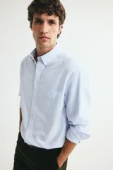 Camisa de algodón H&M Oxford con estampado de rayas verticales celestes y blancas, cuello americano, bolsillo en el pecho y manga larga.