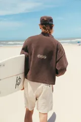 Buzo de tejido de punto color marrón con cuello polo, manga larga y estampado frontal con el nombre de la marca en color crema.