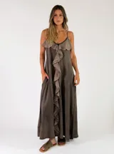 Vestido largo sin mangas de color marrón con efecto gastado, tirantes finos, escote en V con volados y gran volante central delantero que recorre toda la prenda. Cuenta con bolsillos laterales.