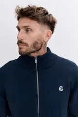 Cardigan de punto color azul marino, con cierre frontal completo, cuello alto y puños acanalados. Presenta un pequeño bordado distintivo en el pecho.