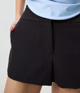 Micro short de sastrería negro, de tiro alto y corte ajustado, confeccionado en poliéster con elastano, con pretina ancha cruzada en el delantero.