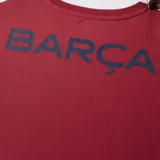 Camiseta deportiva color borgoña con cuello redondo y mangas cortas. Estampado en el pecho con el escudo del FC Barcelona y la palabra "Barça" en azul.