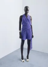 Vestido corto cruzado sin mangas, de color azul con estampado de lunares blancos, escote en V y detalle de lazo lateral.