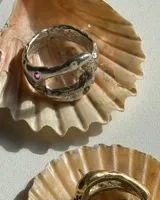 Anillo de plata con diseño orgánico y texturizado, que presenta una pequeña piedra incrustada de color rosado.