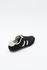 Zapatilla urbana de perfil bajo con diseño retro, confeccionada en poliuretano con detalles en textura tipo gamuza. Presenta puntera redondeada, cordones clásicos y suela de goma color caramelo.