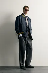 Cazadora bomber estilo universitario, de corte relaxed fit y tejido técnico azul marino, con cuello, puños y dobladillo de rib elástico a rayas amarillas. Cuenta con bolsillos delanteros de plastrón y cierre frontal con botones a presión.