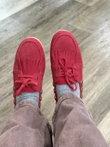 Náuticos de gamuza color rojo con flecos en la parte delantera, cordones al tono y detalle de tachas metálicas en los laterales.